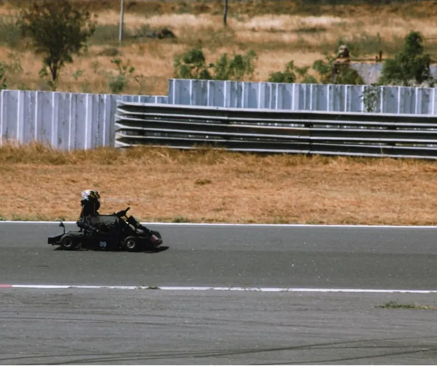 The kart on the far side of the circuit with the treeline behind it.